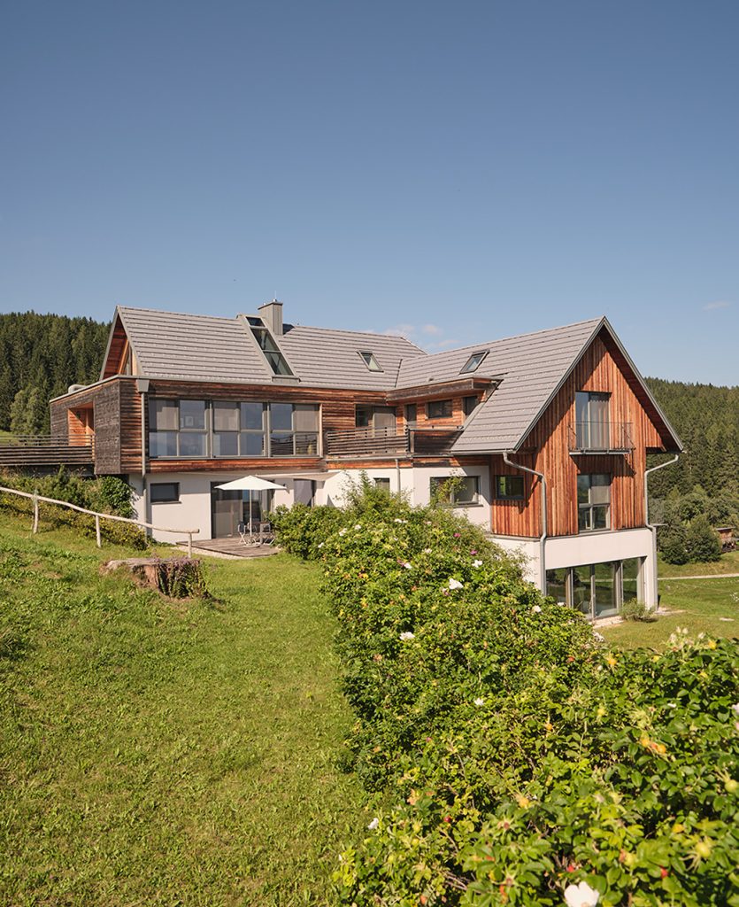 The JK7® Spa & Wellness retreat, a wood-clad alpine house on a green hillside backed by forested mountains in Carinthia.