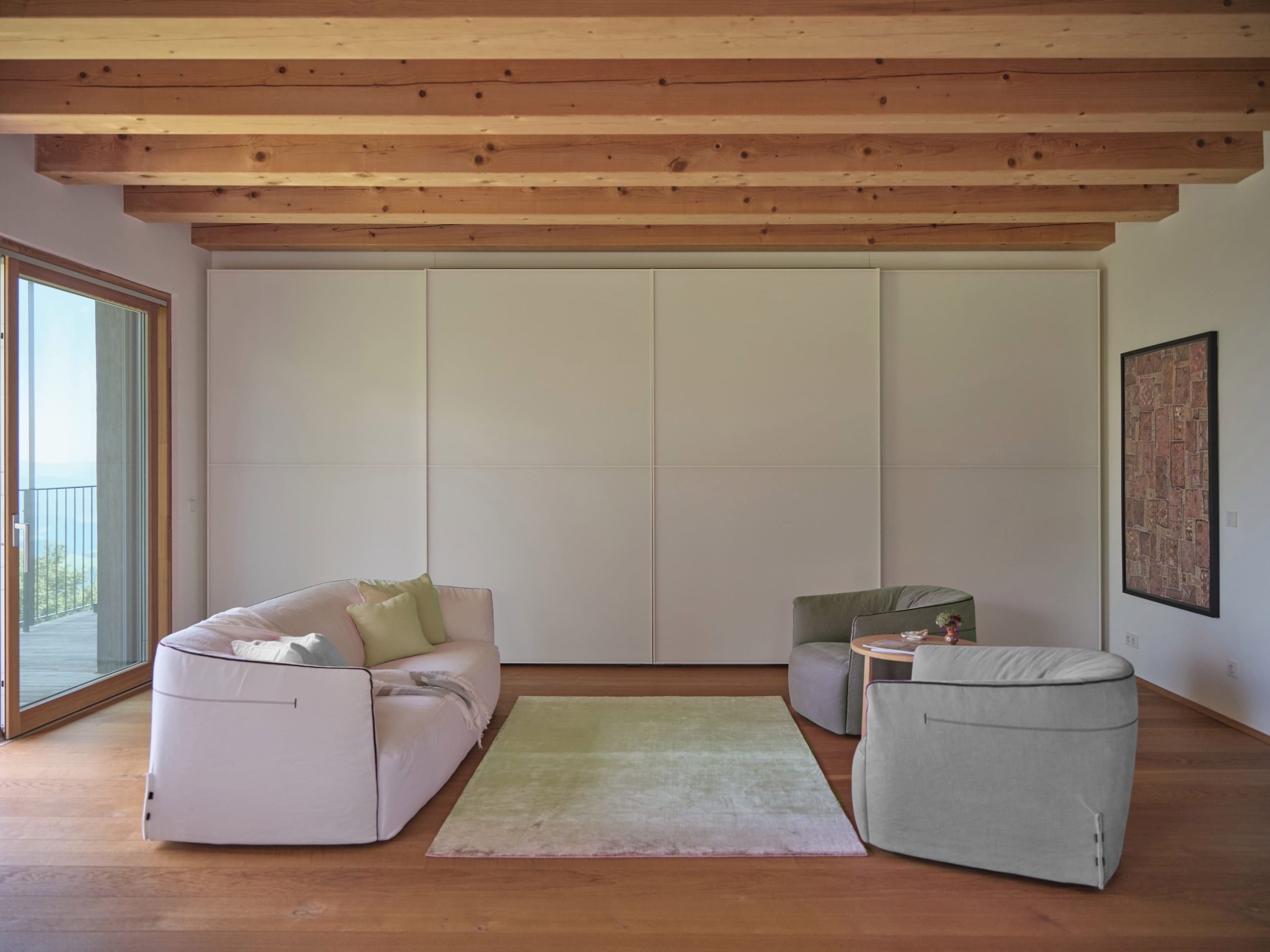 Minimalist living room with a plush sofa, sage green armchairs, and rustic wooden ceiling beams.