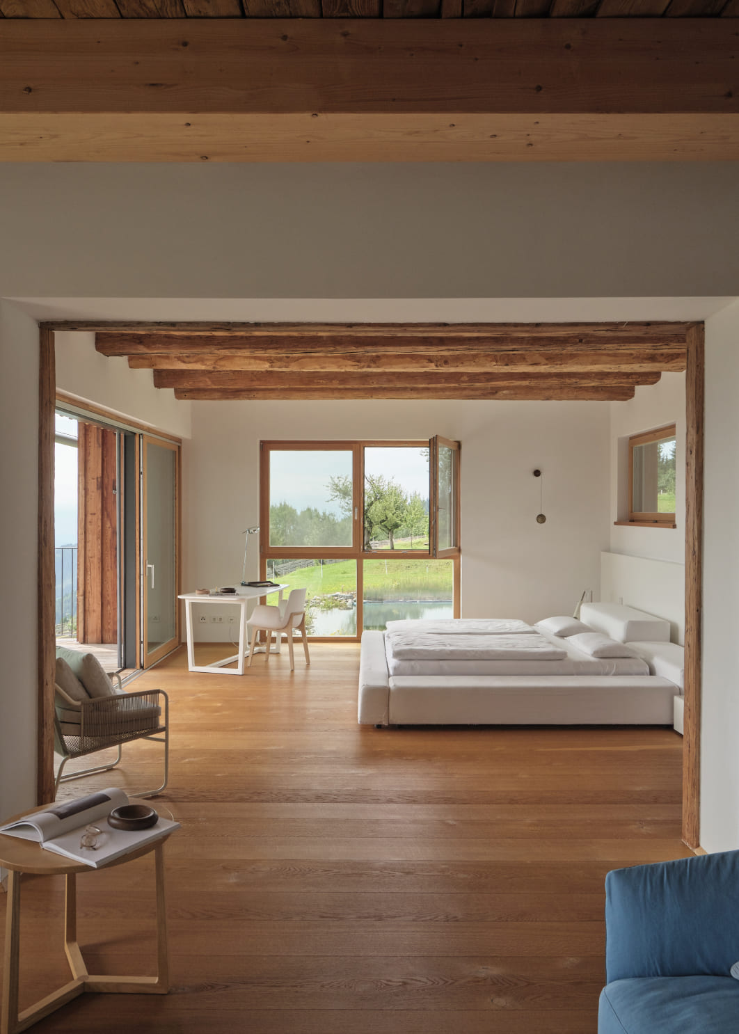 Spacious luxury suite with a minimalist bed, workspace, and large windows overlooking an impressive mountain range.